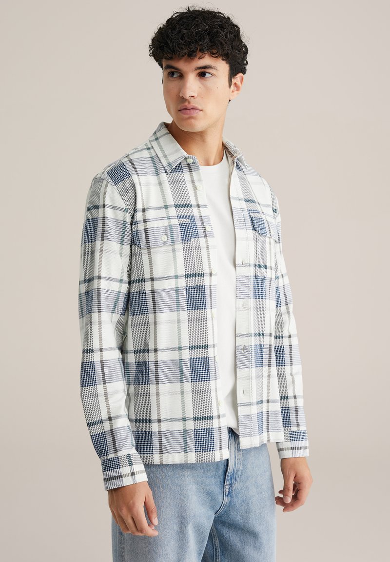 Ruudullinen paita valkoisena, sinisenä ja vihreänä, jossa on napillinen etuosan suunnittelu, kaksi rintataskua ja pitkät hihat, joissa on napilliset kalvosimet.