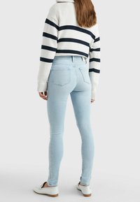 Světle modré skinny džíny s vysokým pasem, které jsou kombinovány s bílo-námořnickým pruhovaným svetrkem na crop, a bílými slip-on botami.