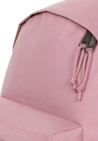 Mochila de tela rosa con material texturizado, tapa plegable y cierre con cremallera, decorada con cuerdas y tiradores metálicos.