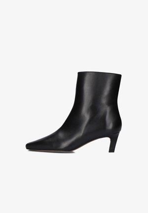 Bottine en cuir noir avec un bout pointu et un petit talon. Texture lisse, design minimaliste et silhouette hauteur de cheville.