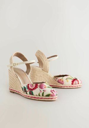 Sandaletter med kilehæle, vævet jutehælg, blomsterbroderet overdel i elfenben og justerbar ankelrem i en lys beige farve.