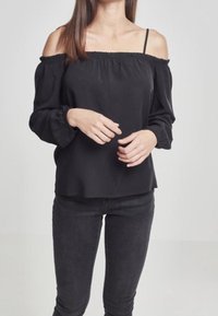 Mustat olkaimeton paita, jossa on joustava kaula-aukko, pitkät hihat joustavilla hihansuilla ja sileä kangas; yhdistetty mustiin kapeisiin farkkuihin.