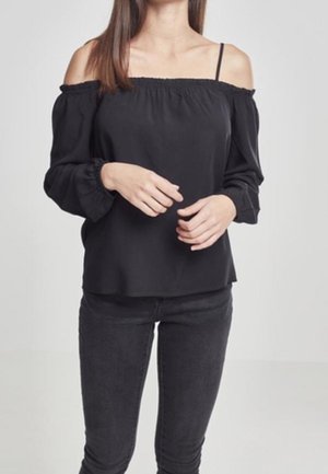Schwarze schulterfreie Bluse mit elastischem Ausschnitt, langen Ärmeln mit elastischen Bündchen und glattem Stoff; getragen mit schwarzen Skinny-Jeans.