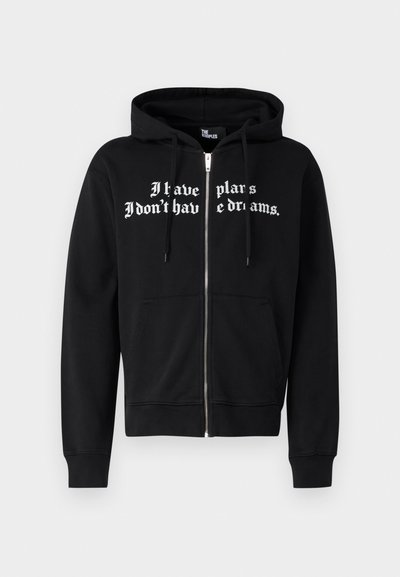 Melna jaku ar rāvējslēdzēju, ar priekšējo kabatu, šņorējamu kapuci un baltu tekstu "Man ir plāni, man nav sapņu."