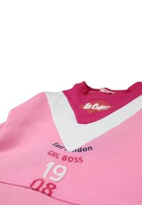 Sweatshirt rose avec des accents blancs, présentant un col en V, un texte brodé "East London GIRL BOSS" et un logo graphique. Texture en coton douce.