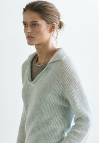 Maglione azzurro chiaro lavorato a maglia con scollo a V profondo e ampio colletto, caratterizzato da una texture morbida e una vestibilità ampia, sovrapposto a un top color taupe.