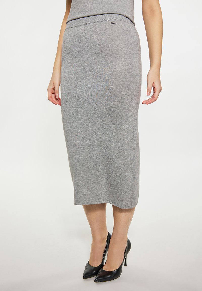 Grijze ribgebreide midi-skirt met een aansluitende taille en recht silhouet, gecombineerd met puntige zwarte hakken.