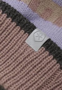 Stickad mössa med ribbat mönster i rosa och grått, med en silverfärgad logotagg. Texturen verkar mjuk och varm, lämplig för kallare väder.