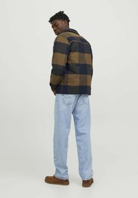 Miestenska károvaná košeľa bunda v tmavomodrých a hnedých odtieňoch, so golierom, gombíkovou légou a mäkkou textúrovanou tkaninou. Skombinovaná so svetlomodrými džínsami.