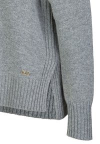 Grijze gebreide trui met ribbeltextuur en zijslits. Bevat een klein gouden logo-label nabij de zoom. Zacht materiaal; ontspannen pasvorm.