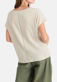 Top corto de color beige claro con mangas cortas y un escote redondo, adornado con una línea cosida a lo largo del centro de la espalda. Tela suave y texturizada.