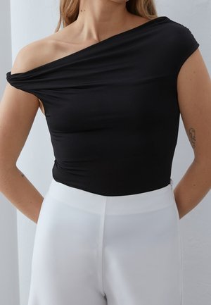 Body negro sin hombros de tela suave, con un silueta ajustada. Combinado con pantalones blancos de talle alto, creando un contraste moderno.