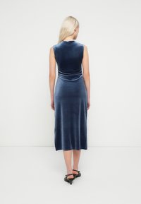 Hihaton samettinen mekko syvänsinisenä, jossa istuva yläosa ja liehuva midipitkä hame. Hienovarainen kiilto ja sivuhalkio.