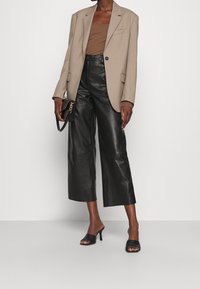 Beige kavaj över en brun topp, ihop med högmidjade svarta läderbyxor med vida ben och svarta öppna klackar. Svart handväska med kedjedetalj.