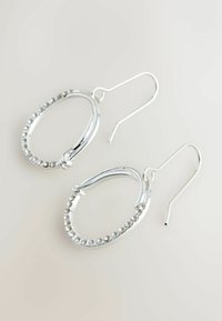 Pendientes de aro de plata con un exterior suave y una fila de piedras preciosas transparentes a lo largo del borde. Cierre de gancho para un uso seguro.