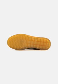 Semelle en caoutchouc transparente avec une surface structurée, dotée d'une finition teintée de jaune et d'un design texturé pour une meilleure adhérence.