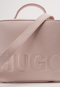 Borsa in pelle rosa con finitura texture, caratterizzata da un logo moldato e una tracolla ampia. Include una maniglia superiore per una maggiore praticità nel trasporto.