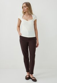 Top di crema chiaro a coste con scollatura quadrata e maniche corte, abbinato a pantaloni aderenti marrone scuro e scarpe basse nere intrecciate.