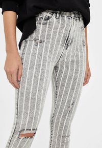 Černobílé pruhované džíny z denimu s opotřebovanými detaily. Vysoký pas, pět kapsový design a mírně vybledlá textura.