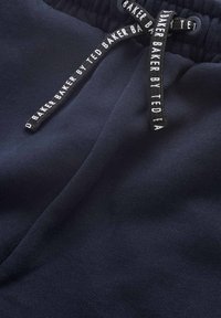Mörkblå joggers i mjukt tyg med elastisk midja. Har svarta snören med vit logotext. Slät yta, avslappnad design.