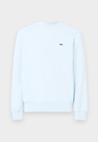 Ljusblå långärmad sweatshirt med rund halsringning, ribbade muddar och fåll, med en liten grön krokodil-logotyp på vänster bröst.