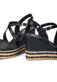Sandales compensées noires avec un design à lanières croisées, fabriquées en matériau synthétique texturé et dotées d'une semelle en jute tressé. Détail en métal doré.