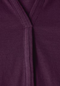 Maglietta a scollo a V in tessuto viola intenso con una texture liscia e cuciture visibili lungo le cuciture, che evidenziano il design elegante.