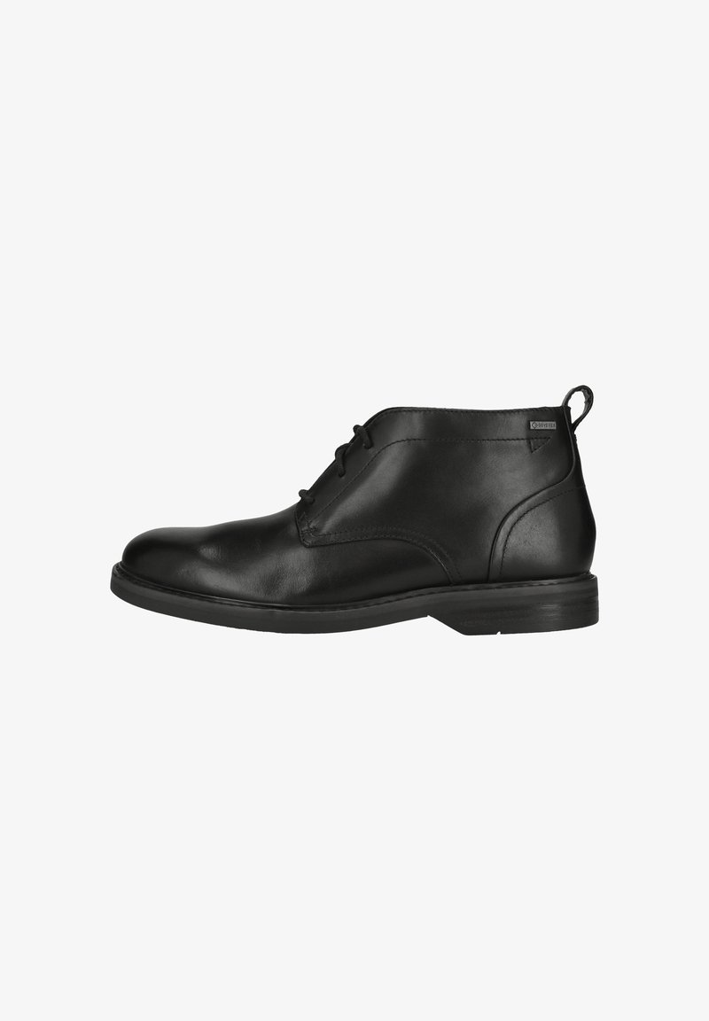 Bottine en cuir noir avec trois œillets, bout arrondi, languette de tirage à la cheville et semelle lisse sur fond blanc.