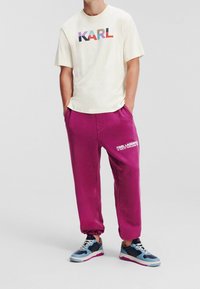 Light cream t-shirt with multicolored "KARL" print, paired with pink sweatpants featuring white text. Blue and black sneakers complete the outfit.