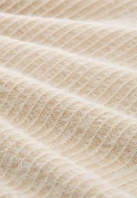 Gewebter Stoff in hellem Beige mit einem subtilen Wellenmuster, das eine weiche Textur und fuzzy Oberflächendetails aufweist.