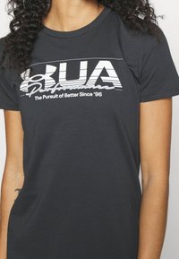 Svart bomullströja med korta ärmar som har djärv vit grafisk text och en rundad logotyp. Slät textur, klassisk rund halsringning.