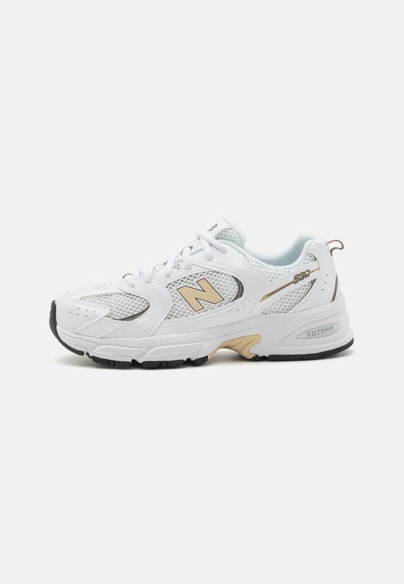 Baskets New Balance 530 blanches et or avec panneaux en mesh, conception à lacets, et semelle en caoutchouc noire et beige sur fond uni.