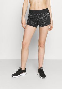 Czarne szorty z teksturowanym wzorem białych trójkątów, wyposażone w szeroki czarny pas. Połączone z czarnymi butami sportowymi na białej podeszwie.