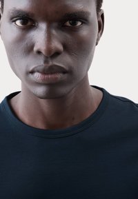 Nahaufnahme eines Mannes, der ein dunkelmarineblaues Baumwoll-T-Shirt mit rundem Halsausschnitt und glatter Textur trägt. Dabei werden seine Gesichtszüge und sein Hautton sichtbar.