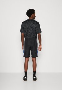 Black graphic t-shirt with a patterned design, paired with black shorts featuring side stripes and branding on the left hem.