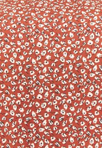 Tissu de couleur rouille avec de petites fleurs blanches et des contours noirs dispersés uniformément dans un motif floral répétitif.