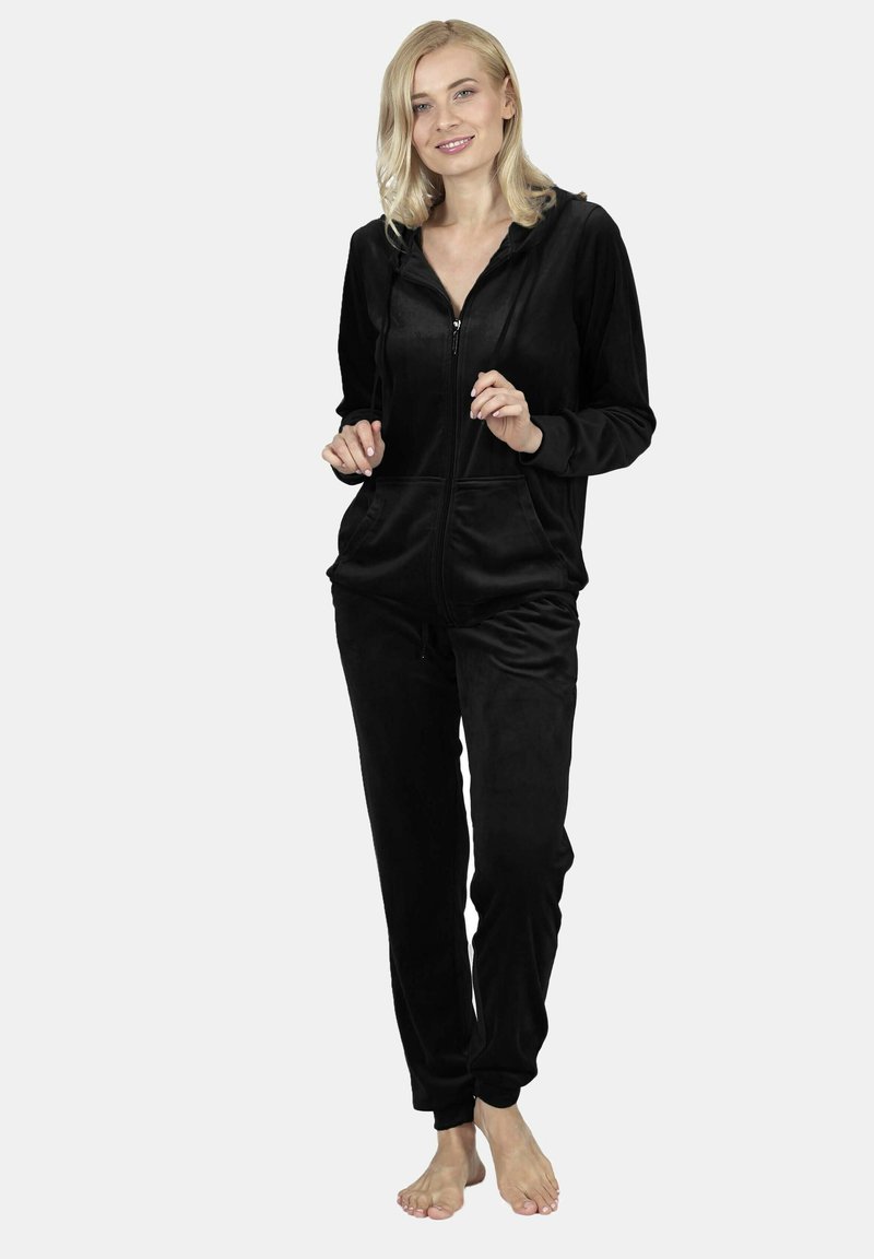 Black velour tracksuit featuring a zip-up hoodie, front pockets, and tapered pants with elastic cuffs. Soft texture, fitted design.
