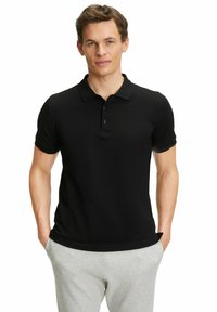 Czarna koszulka polo z krótkim rękawem i zapięciem na guziki, wykonana z gładkiego materiału. Noszona z jasnoszarymi spodniami dresowymi, podkreślająca prosty design.