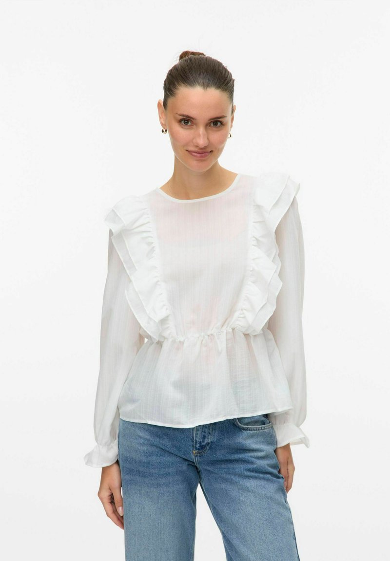Blusa bianca con rifiniture arricciate, vita elastica, maniche lunghe e tessuto trasparente, abbinata a jeans blu. Design semplice ed elegante.