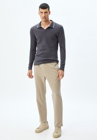 Donkergrijze polo shirt met lange mouwen en een geribbelde structuur, voorzien van een brede kraag met witte accenten, gecombineerd met beige broek en tan sneakers.