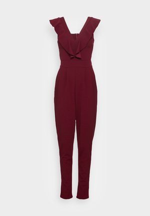 Ærmeløs dyb burgunder jumpsuit med flæset V-udskæring og tætsiddende talje, tilspidsede ben, vist mod en ensfarvet baggrund.