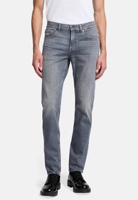Lichtgrijze denim jeans met een recht gesneden fit. Bevat vijf zakken, metalen accenten en subtiele vervaging voor textuur. Draagt met zwarte schoenen.