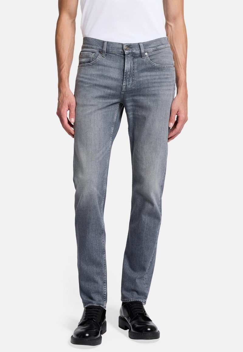 Lichtgrijze denim jeans met een recht gesneden fit. Bevat vijf zakken, metalen accenten en subtiele vervaging voor textuur. Draagt met zwarte schoenen.