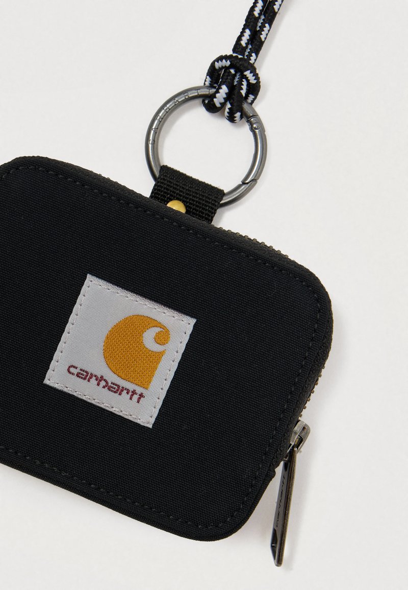 Svart tygfick med dragkedja, en silverfärgad nyckelring och ett flätat band. Har en vit lapp med en gul logotyp och röd text.