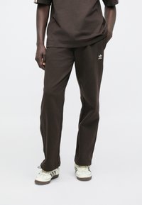 Barna pamutkeverék melegítőnadrág egyenes szárú kialakítással, bal oldalon fehér logóval díszítve, sima tapintású.