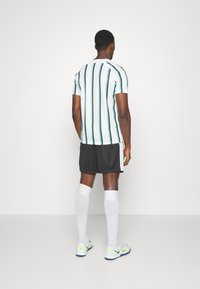 Krátký rukáv, pruhované tričko ve bílé, modré a zelené barvě se černými šortkami, bílými vysokými ponožkami a atletickými botami s neonovými akcenty.