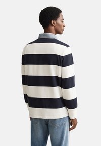 Polo majica z dolgimi rokavi v mornarsko modri in belih vodoravnih črtah. Ima kontrasten jeans ovratnik in sproščen kroj; material iz bombažnega mešanega blaga.