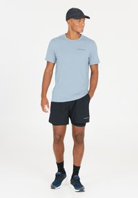 Ljusblå idrottströja, korta svarta sportshorts, svart keps, svarta strumpor och blå sneakers, placerade mot en vit bakgrund.