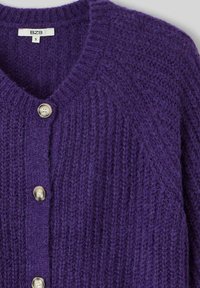 Cardigan en maille violette fait d'un fil doux, avec un col en V et cinq boutons ton argent disposés sur le devant. Design texturé et côtelé.
