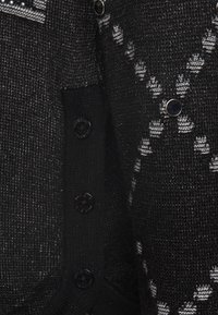 Gros plan d’un tissu en maille noire avec des boutons noirs et un motif losange gris et blanc sur un cardigan texturé.